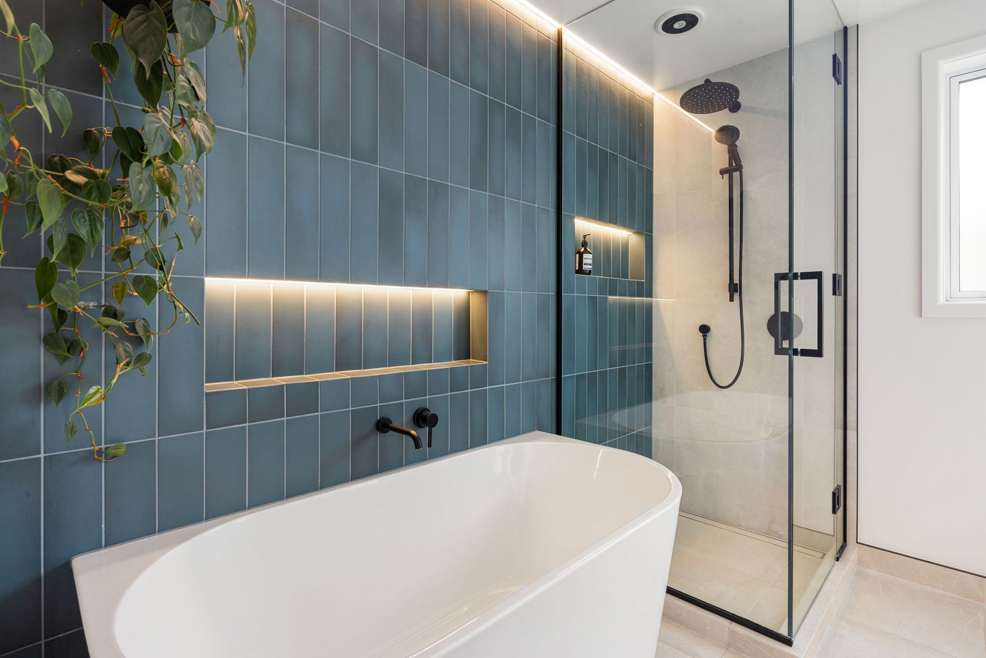 Modern bathroom with teal vertical tiles, white tub, and glass shower.