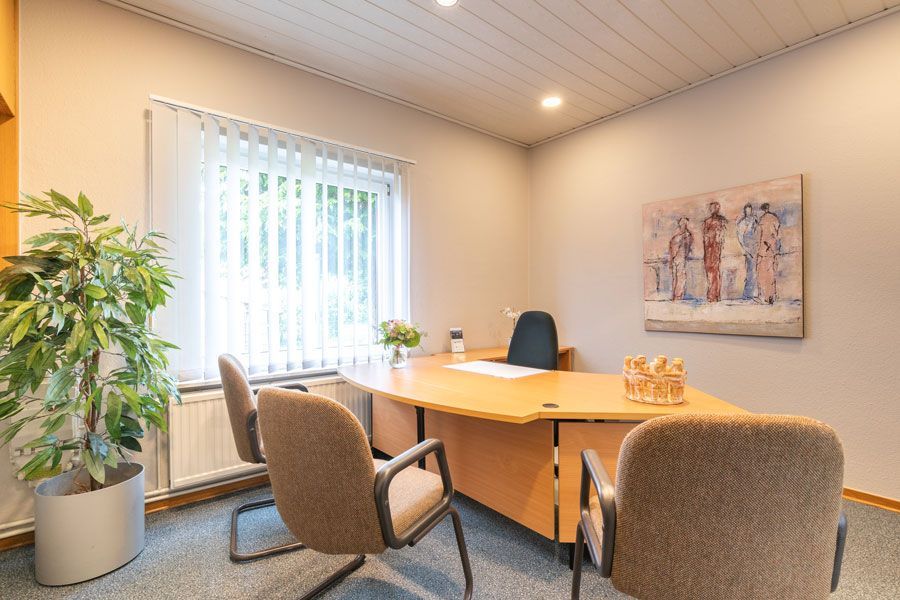 Ein kleines Büro mit einem Schreibtisch, Stühlen und einer Pflanze.