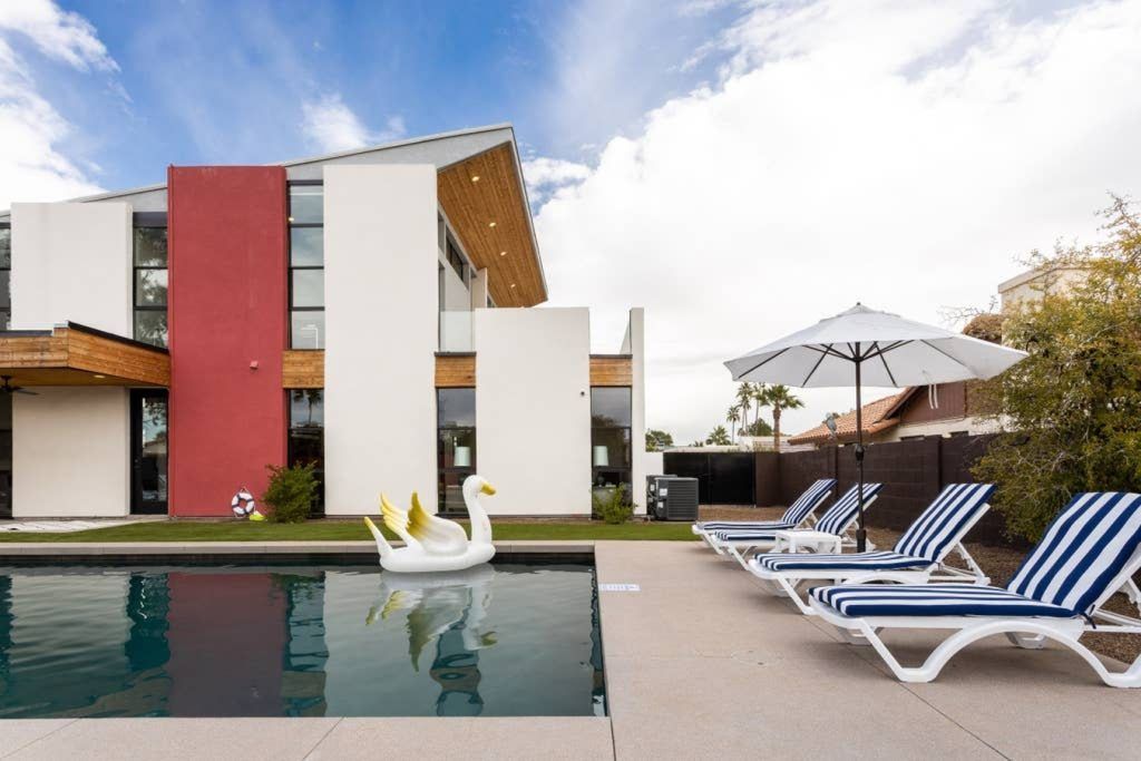 Modern hotel pool with lounge chairs, umbrella, and swan float beside a colorful building