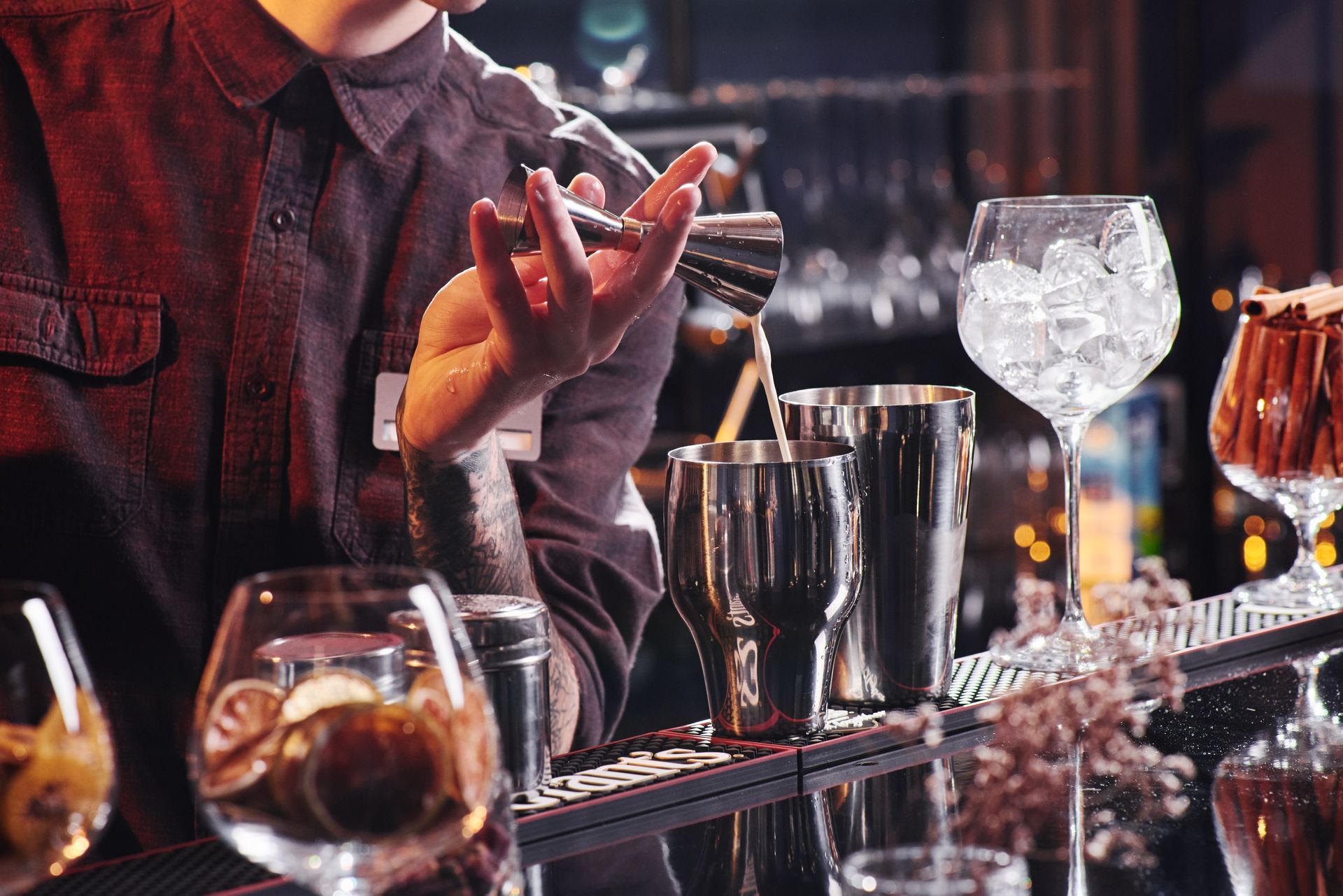 Bartender preparing a cocktail behind a bar with shakers, glasses, and ice