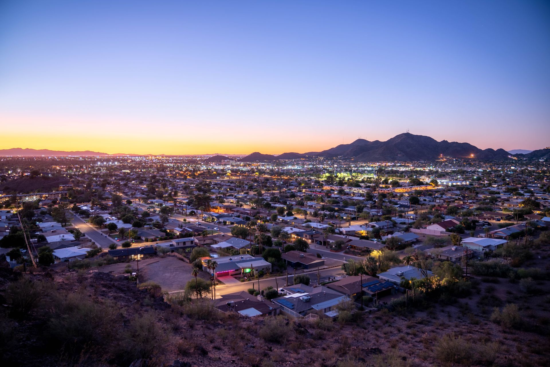 Sunset view over a city with glowing lights and mountains in the distance