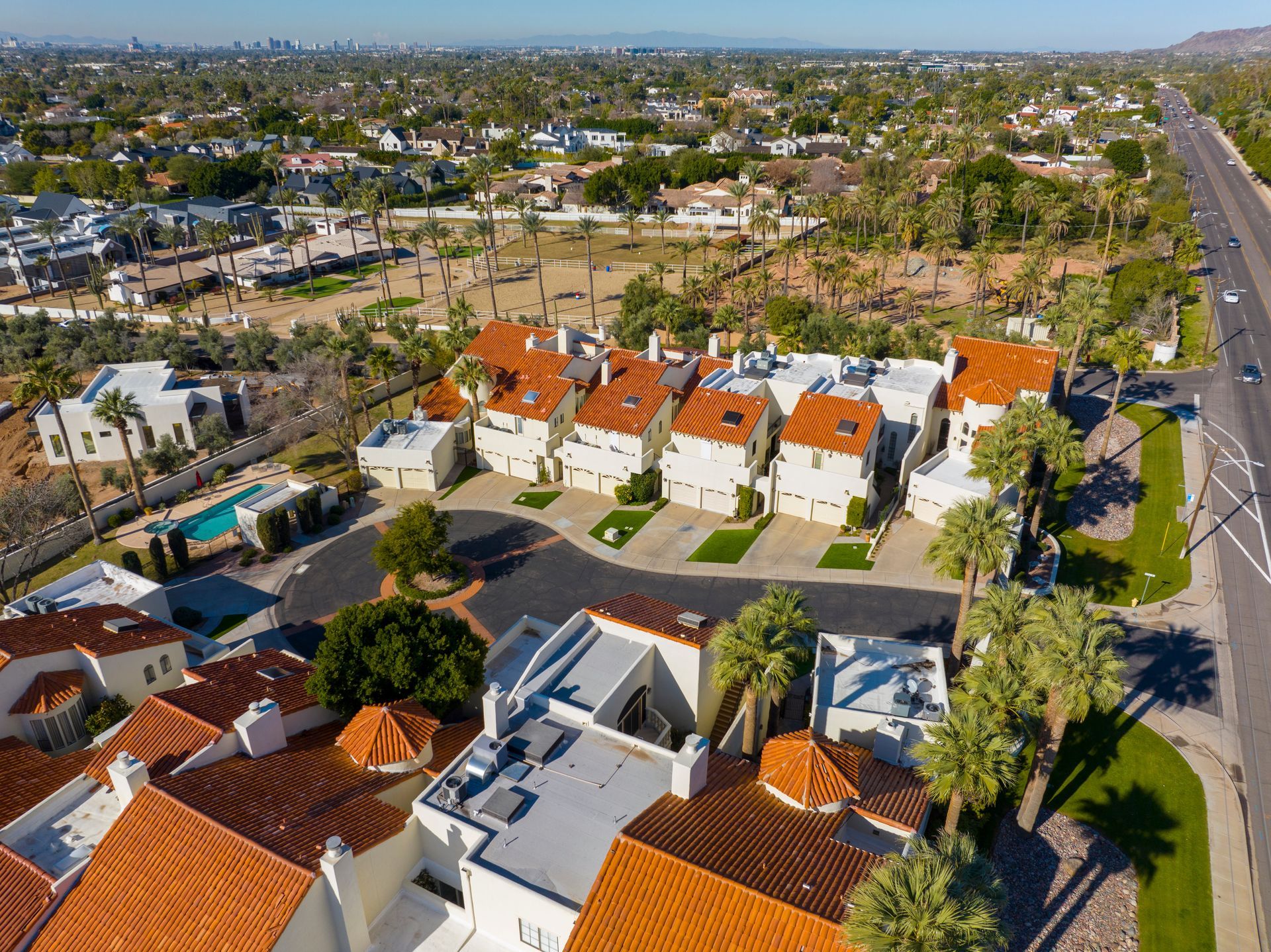 Aerial view of a suburban neighborhood with red-tiled houses and palm trees beside a wide road.