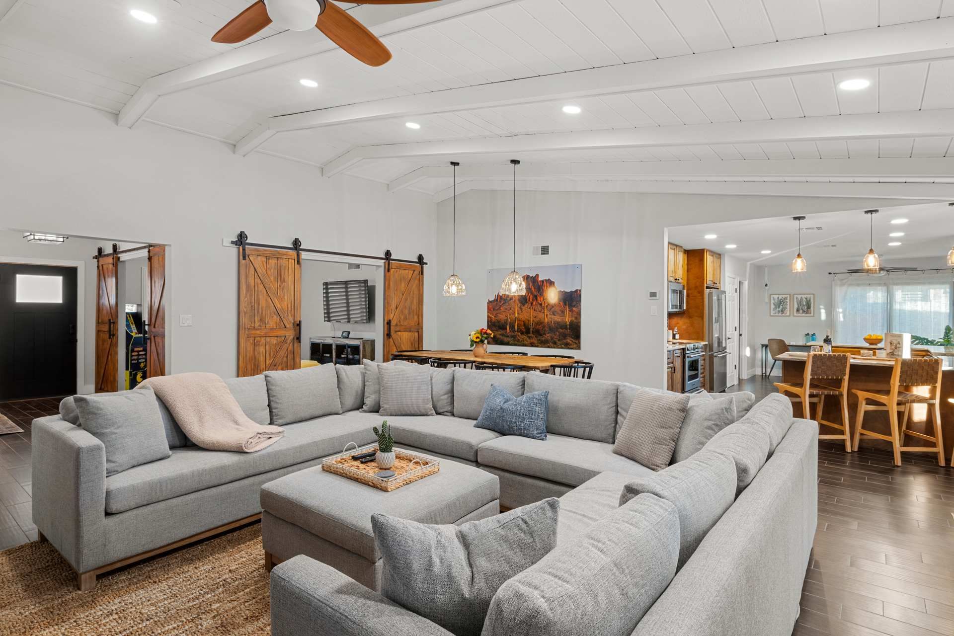 Spacious living room with a large gray sectional, coffee table, wood ceiling fan, and open kitchen-dining area