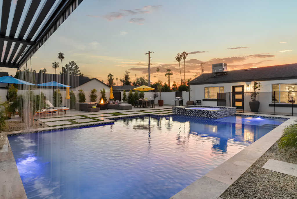 Outdoor swimming pool at sunset with blue lights, lounge chairs, and a modern clubhouse patio