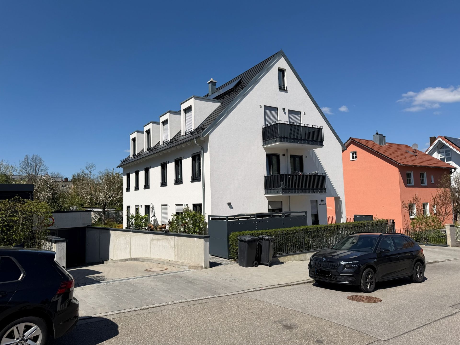Modernes weißes Mehrfamilienhaus mit Balkonen und geparkten Autos an einer sonnigen Straße
