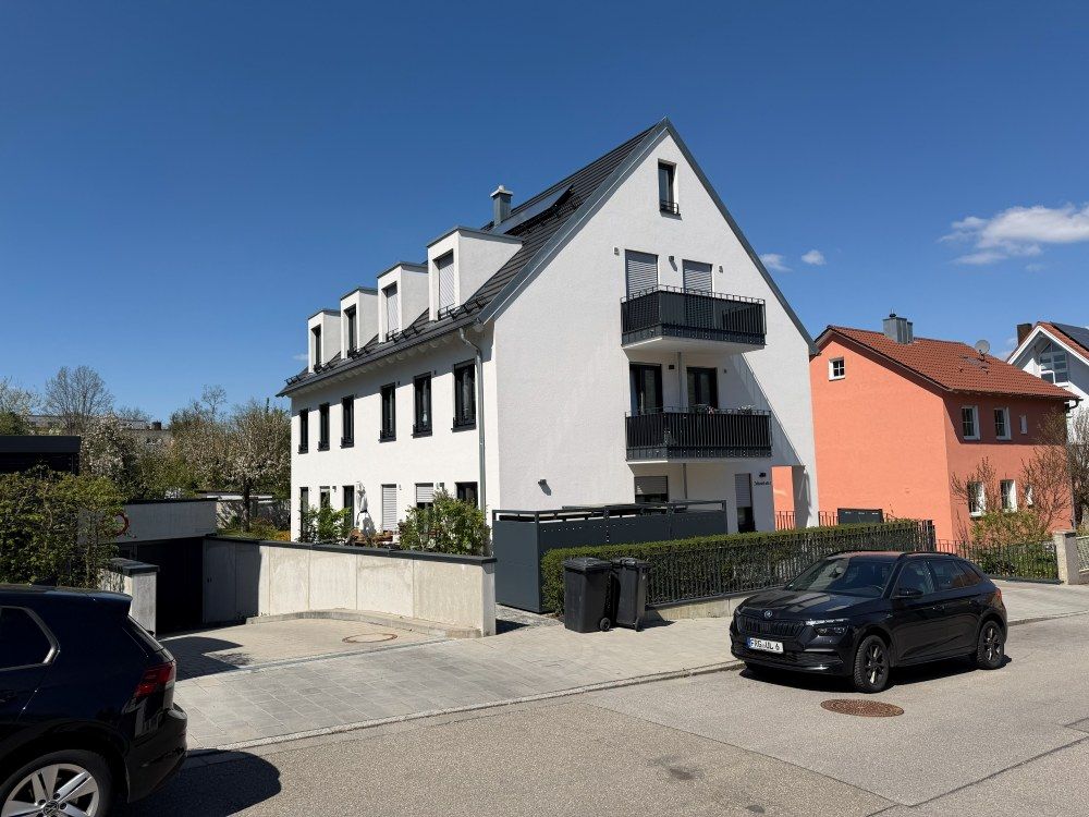 Modernes weißes Mehrfamilienhaus mit Balkonen und geparkten Autos an einer sonnigen Straße