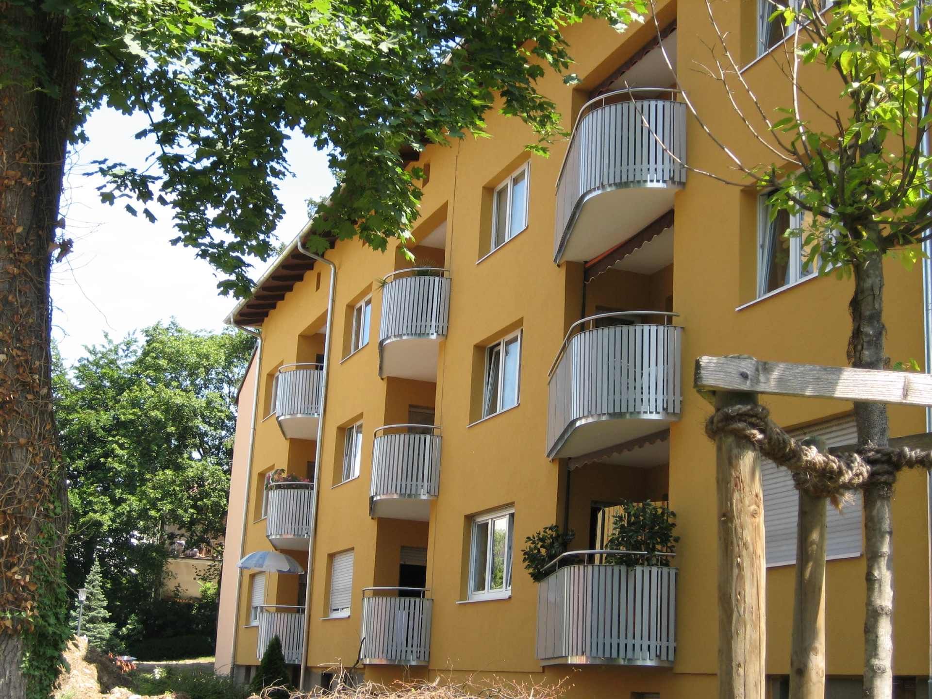 Gelbes Wohnhaus mit geschwungenen Balkonen und Bäumen davor