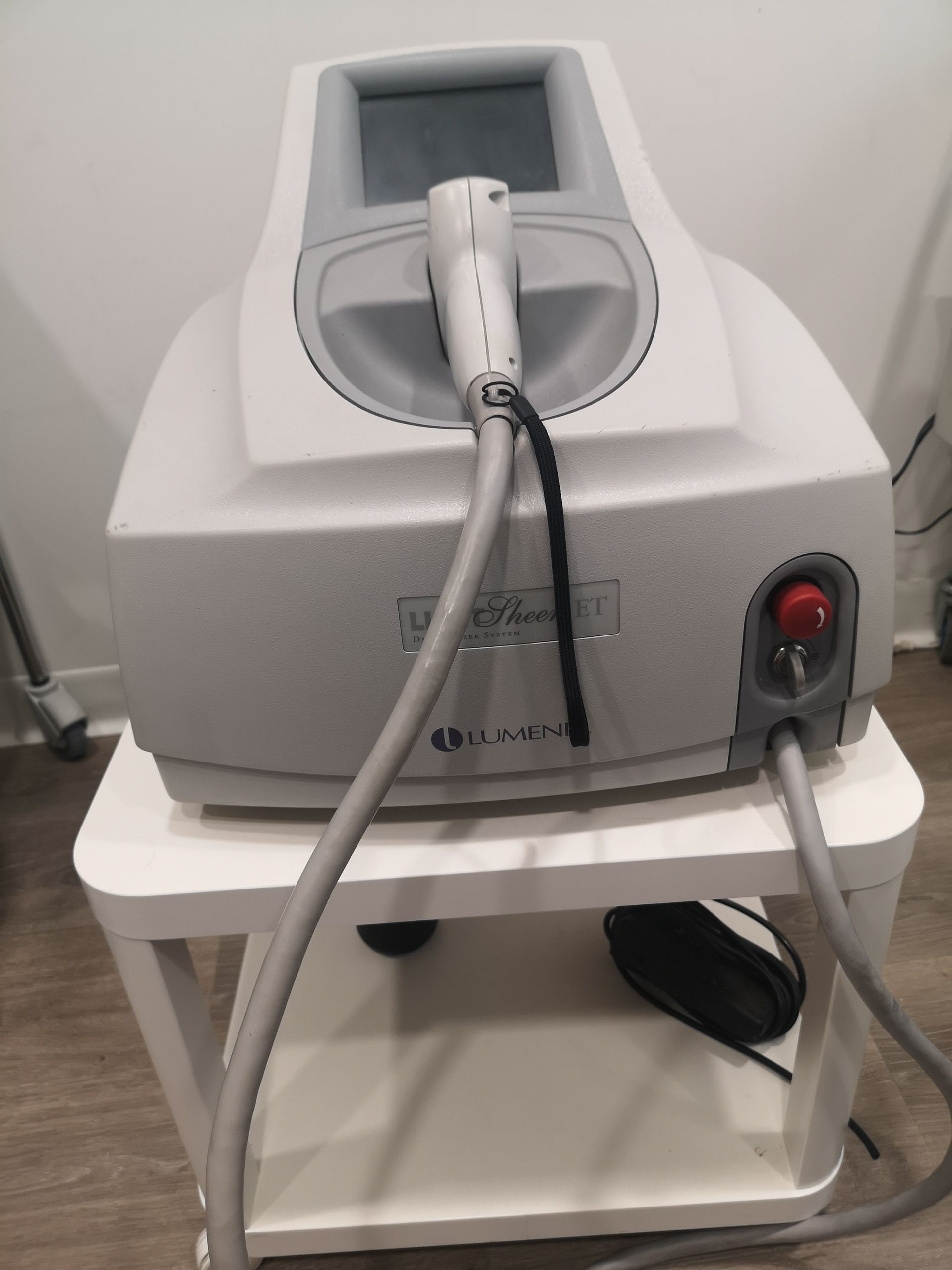 Máquina de depilación láser sobre soporte blanco, de color gris y blanco, con pantalla y pieza de mano.