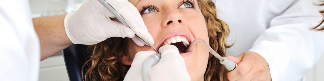 Profesional dental examinando la boca de un paciente con instrumentos y guantes.