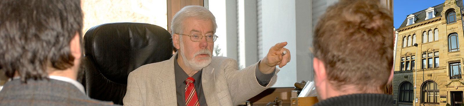 Ein Mann, der auf einem Stuhl sitzt und mit zwei anderen Männern spricht