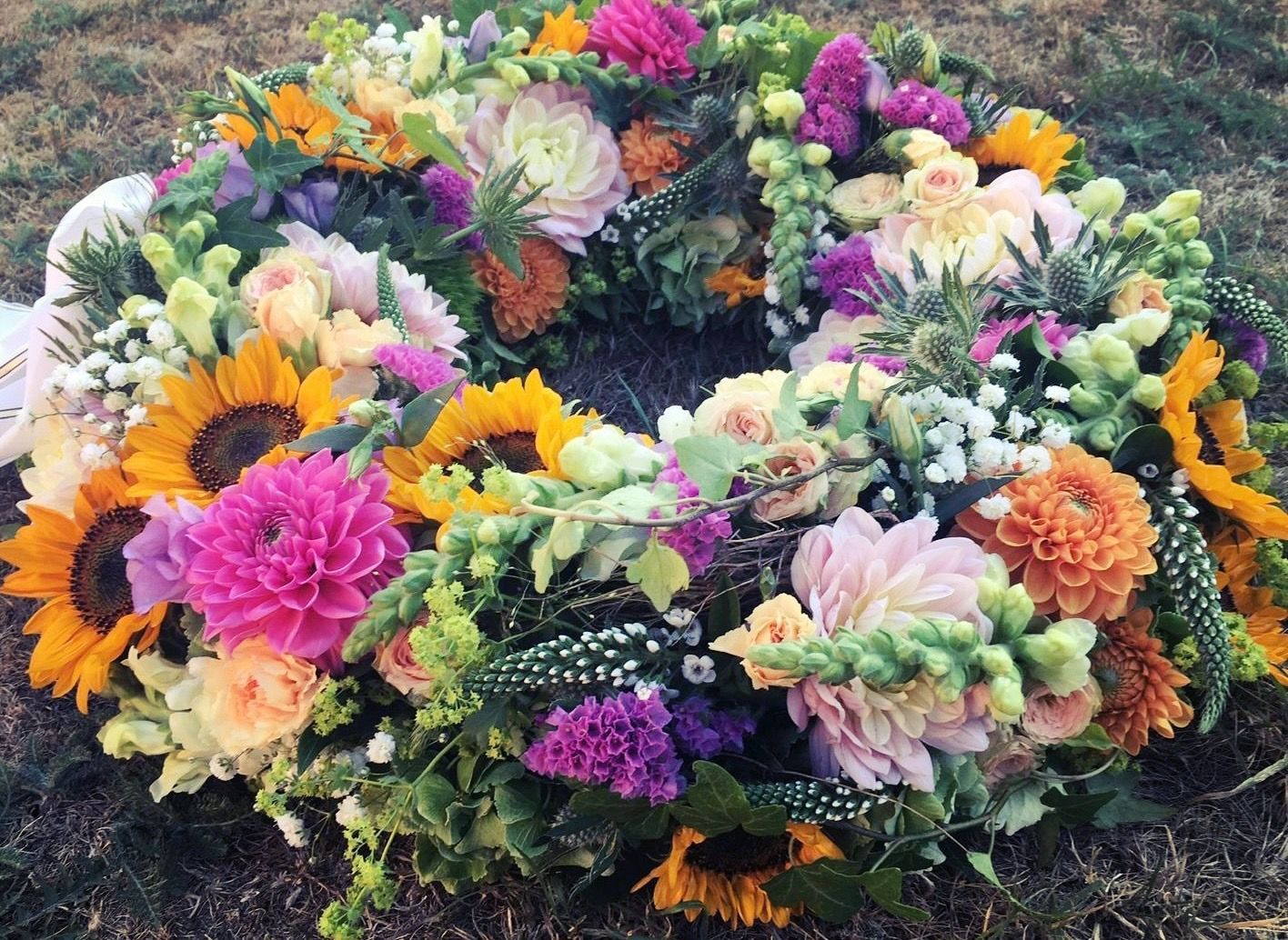 Bunter Blumenkranz auf dem Boden, Sonnenblumen und Dahlien im Vordergrund.