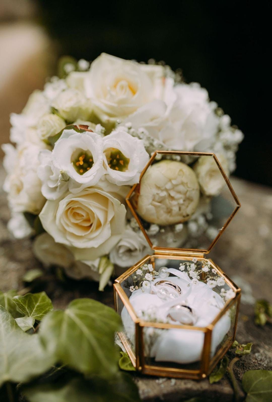 Eheringe in einer geometrischen Glasbox, neben weißen Blumen und Grünpflanzen.