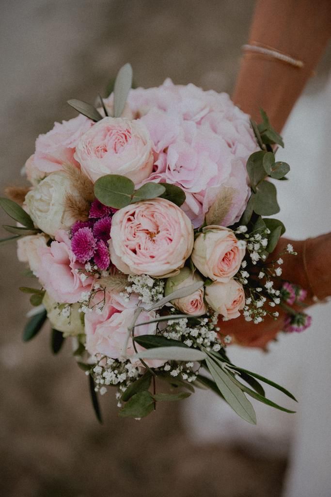 Braut hält einen Strauß rosa und weißer Blumen mit grünem Laub.
