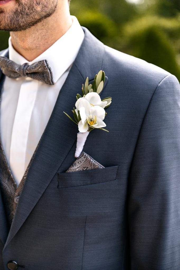 Mann im blauen Anzug mit Fliege, Ansteckblume und Einstecktuch im Freien.