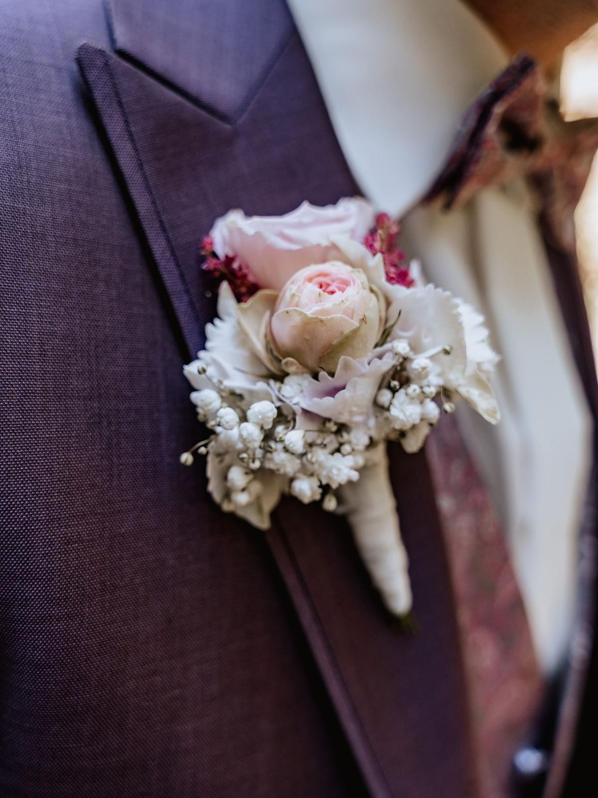 Ansteckblume aus rosa und weißen Blumen, die an einem lila Anzugjackett befestigt ist.