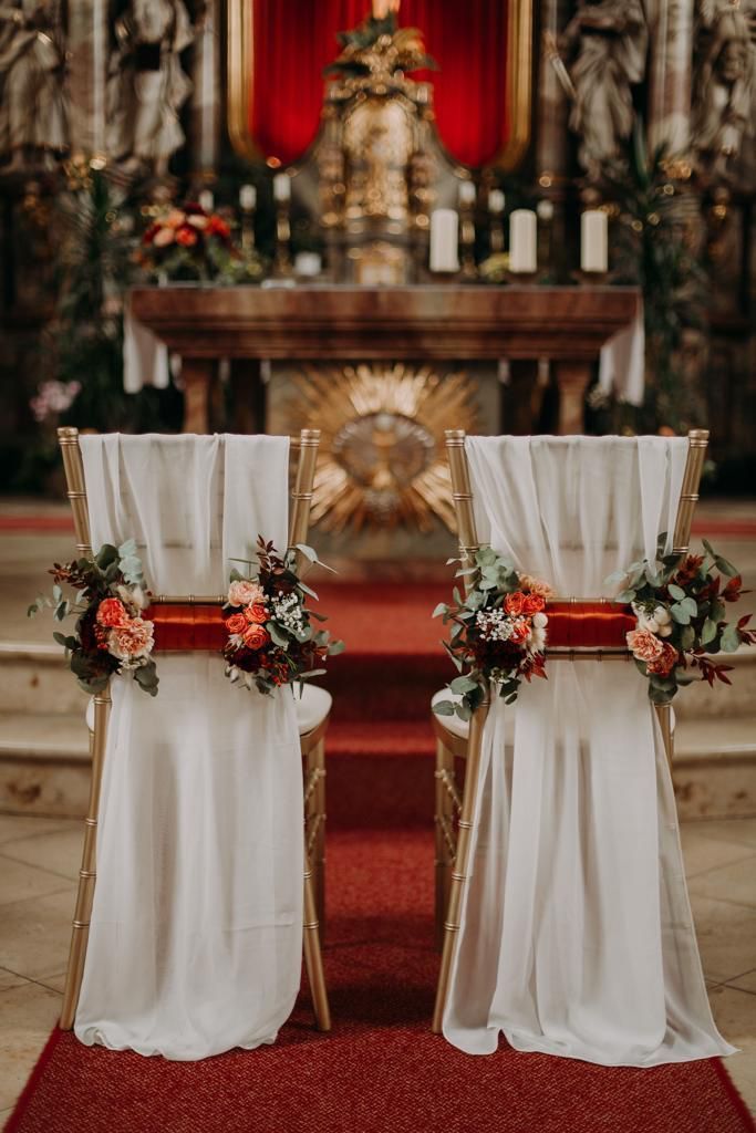 Zwei mit Blumenarrangements dekorierte Stühle warten in einer Kirche auf eine Hochzeitszeremonie.