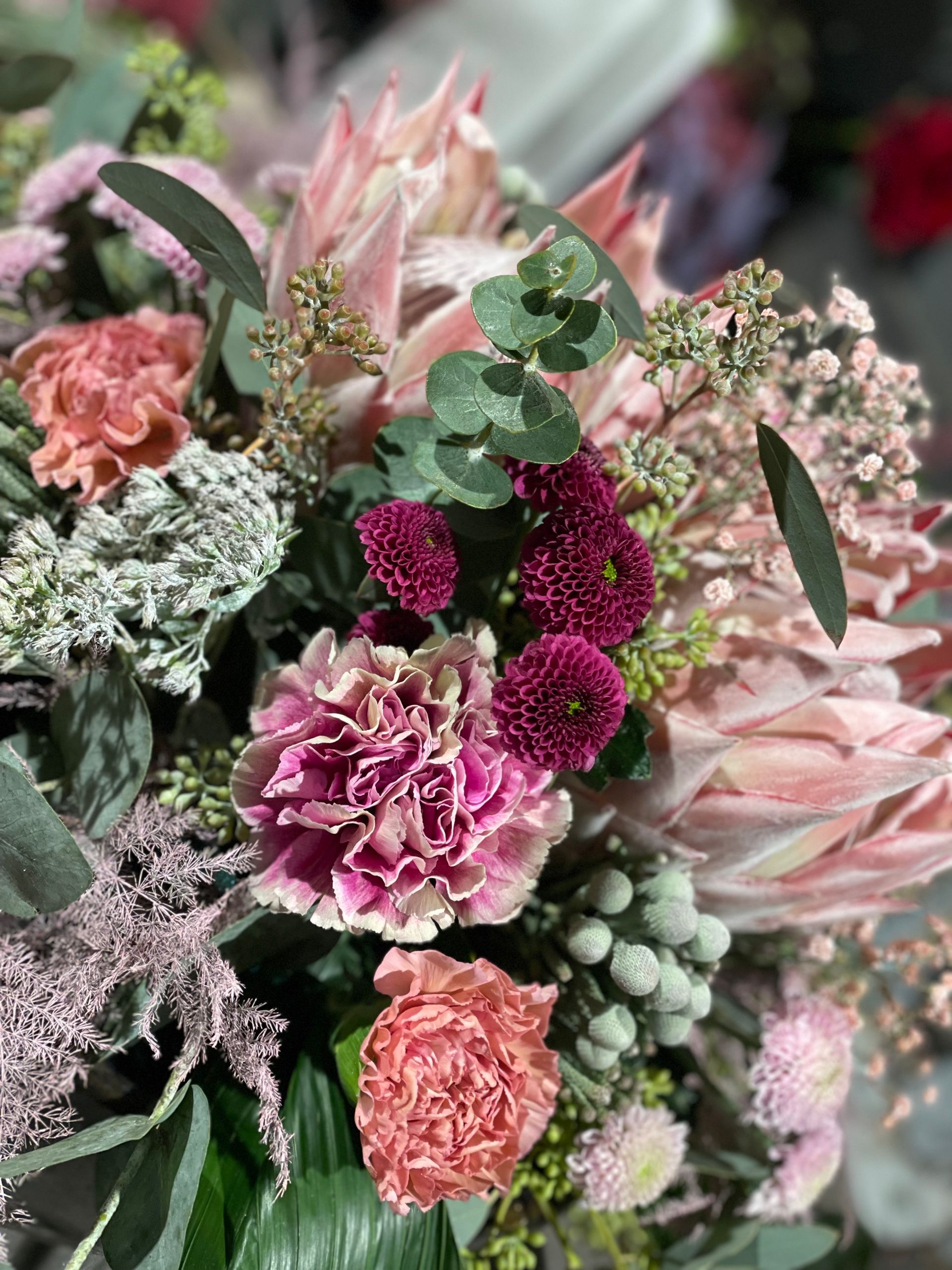 Nahaufnahme eines gemischten Blumenstraußes mit rosa und burgunderfarbenen Blumen, Eukalyptus und Grünpflanzen.