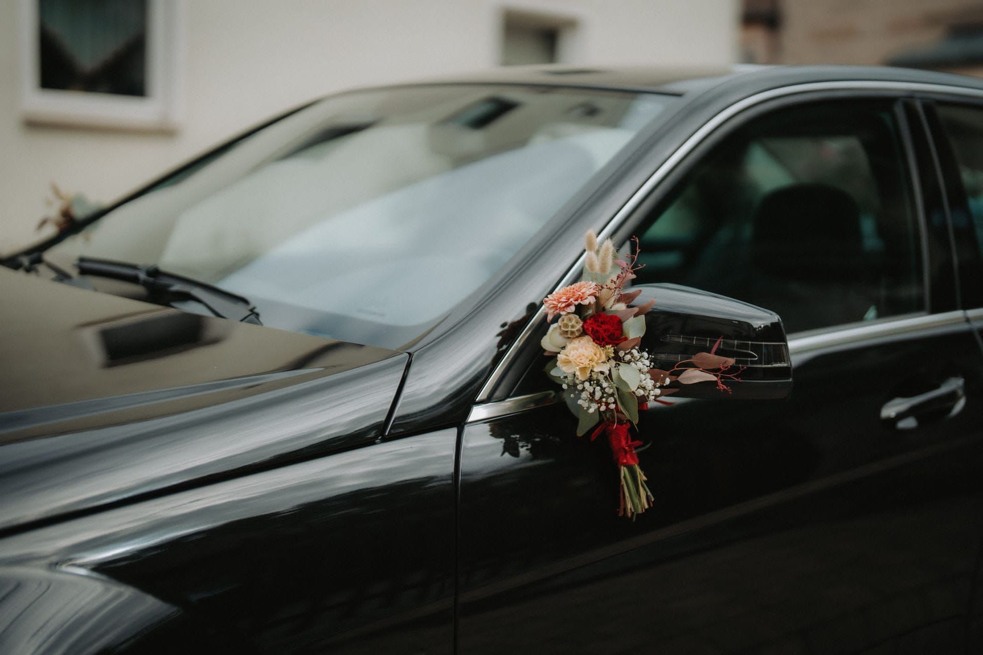 Schwarzes Auto, geschmückt mit einem Blumenstrauß auf dem Seitenspiegel, wahrscheinlich für eine Hochzeit.