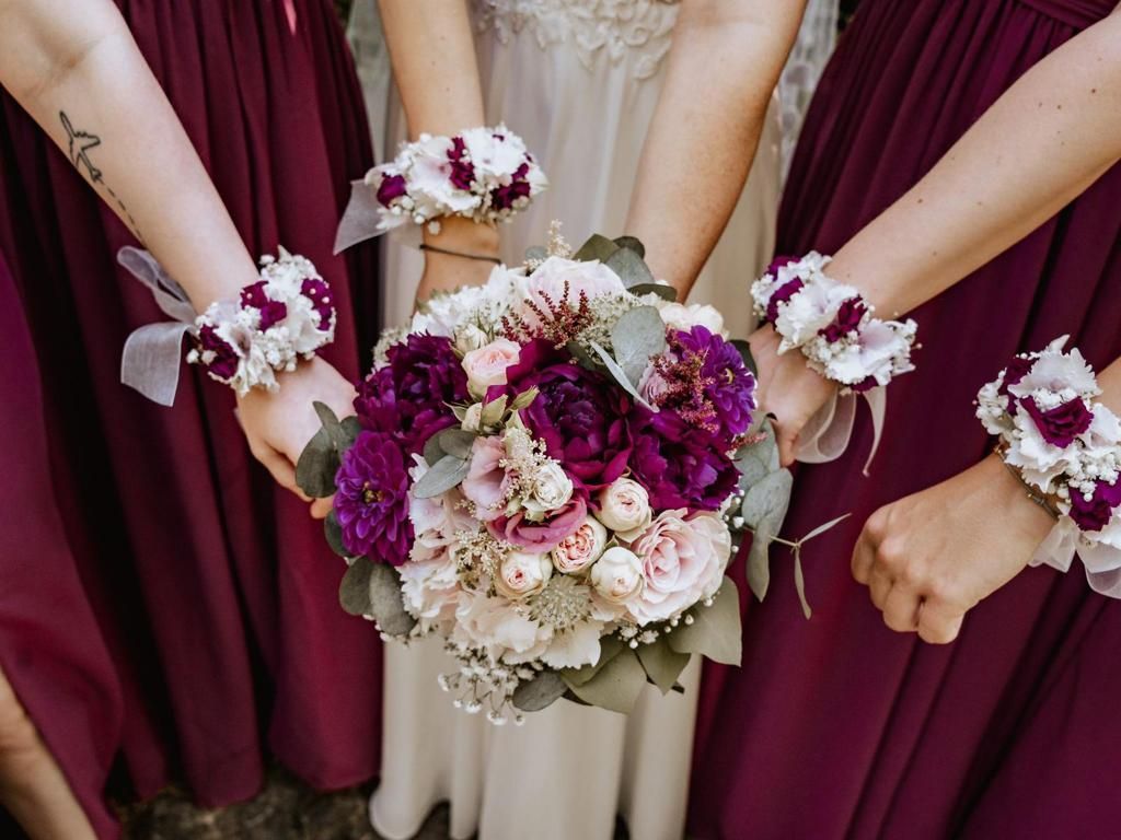 Brautjungfern in burgunderfarbenen Kleidern halten Blumensträuße und Armsträuße mit der Braut.