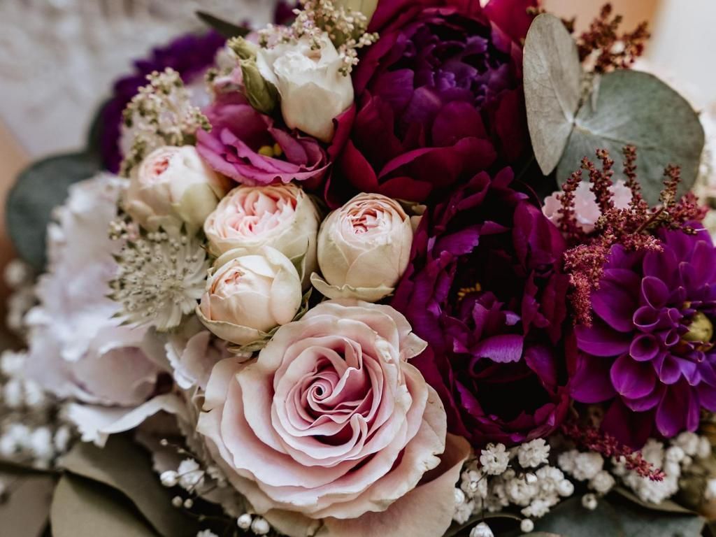 Blumenstrauß aus rosa, violetten und weißen Blumen, darunter Rosen und Pfingstrosen, mit grünem Laub.