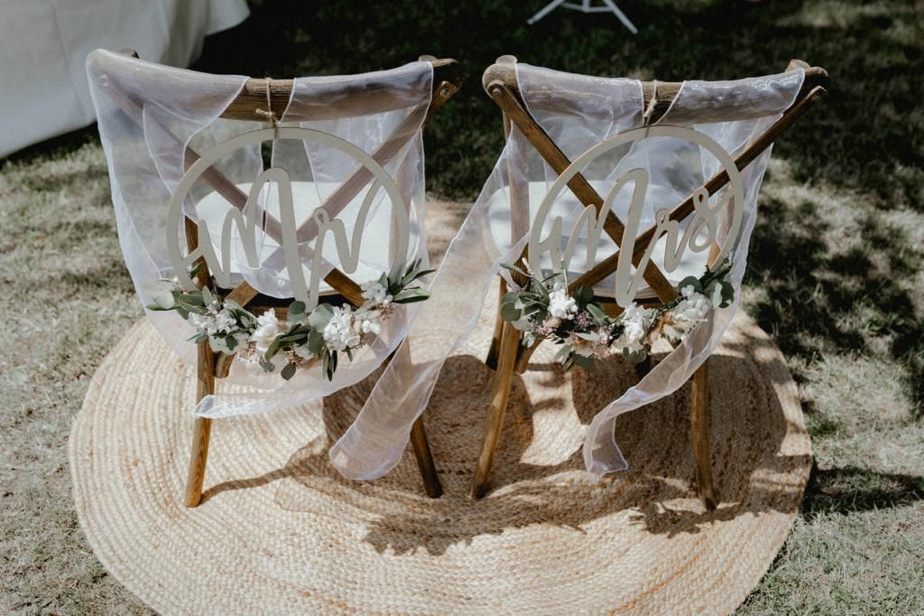 Zwei mit Initialen, Blumen und Stoff verzierte Holzstühle auf einem runden Teppich.