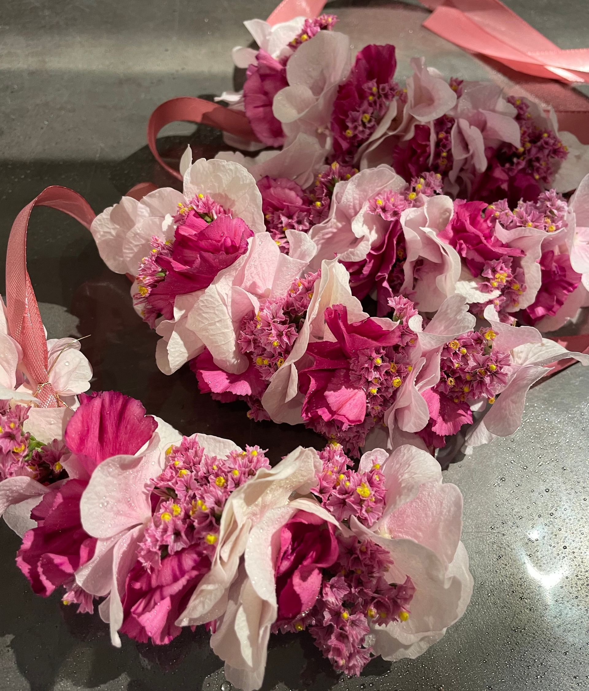 Armsträuße aus rosa und fuchsiafarbenen Blumen mit Bändern, angeordnet auf einer reflektierenden Oberfläche.