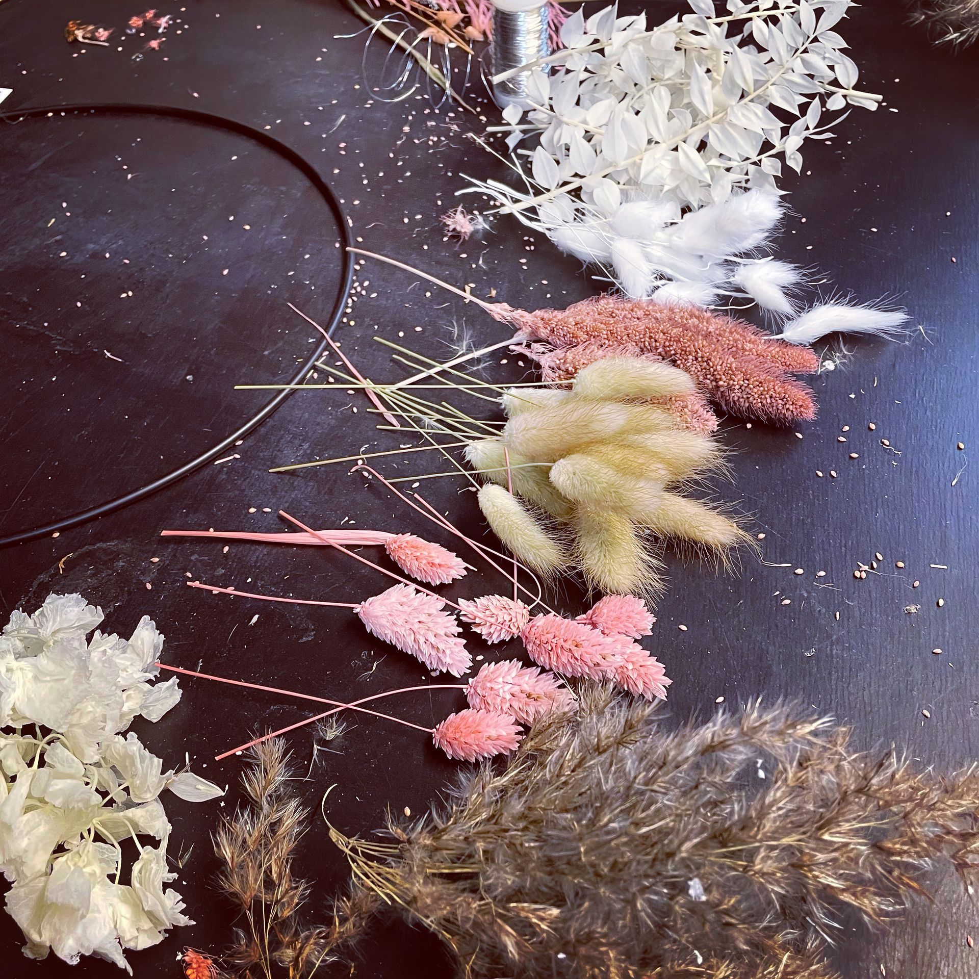 Arrangement aus getrockneten Blumen in verschiedenen Farben, mit einem schwarzen Stirnband, auf einer dunklen Oberfläche.