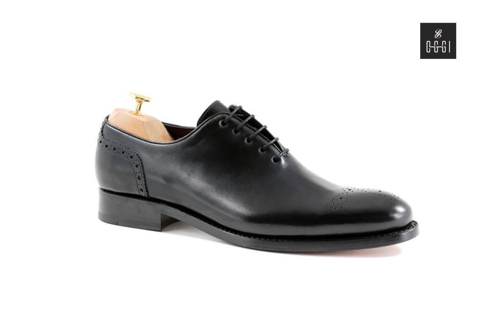 Une paire de chaussures noires avec un porte-chaussures en bois sur fond blanc.