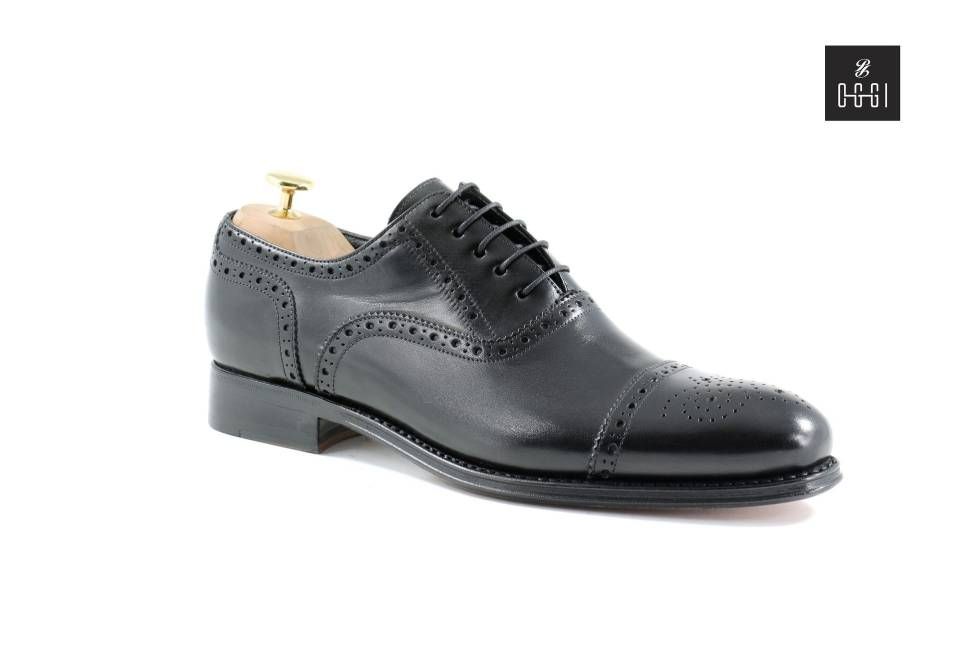 Une paire de chaussures noires avec un embauchoir en bois sur fond blanc.