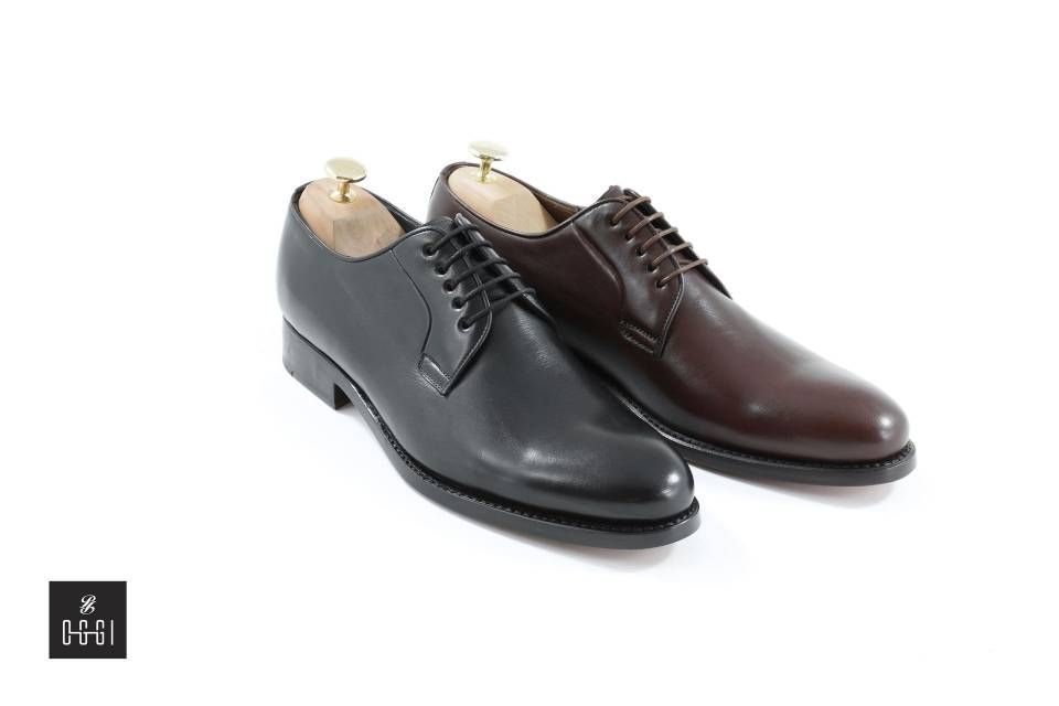 Une paire de chaussures noires et marron avec des embauchoirs en bois sur fond blanc.