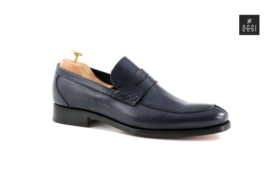 Une paire de mocassins bleus avec un porte-chaussures en bois sur fond blanc.