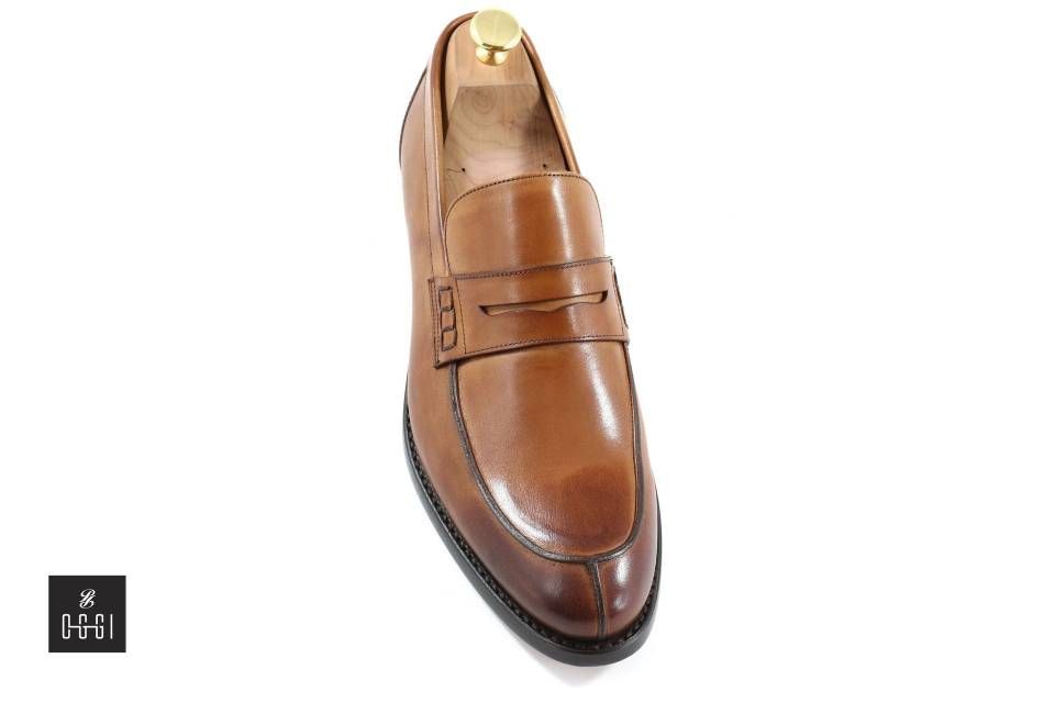 Une paire de mocassins marron avec un porte-chaussures en bois sur fond blanc.