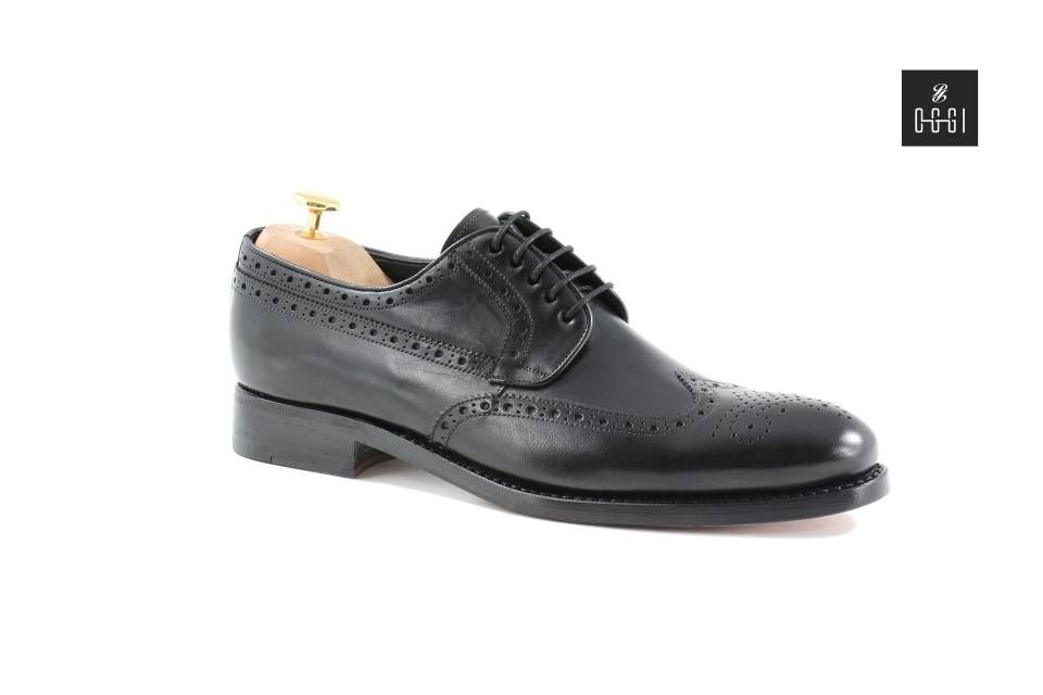 Une paire de chaussures noires avec un porte-chaussures en bois sur fond blanc.