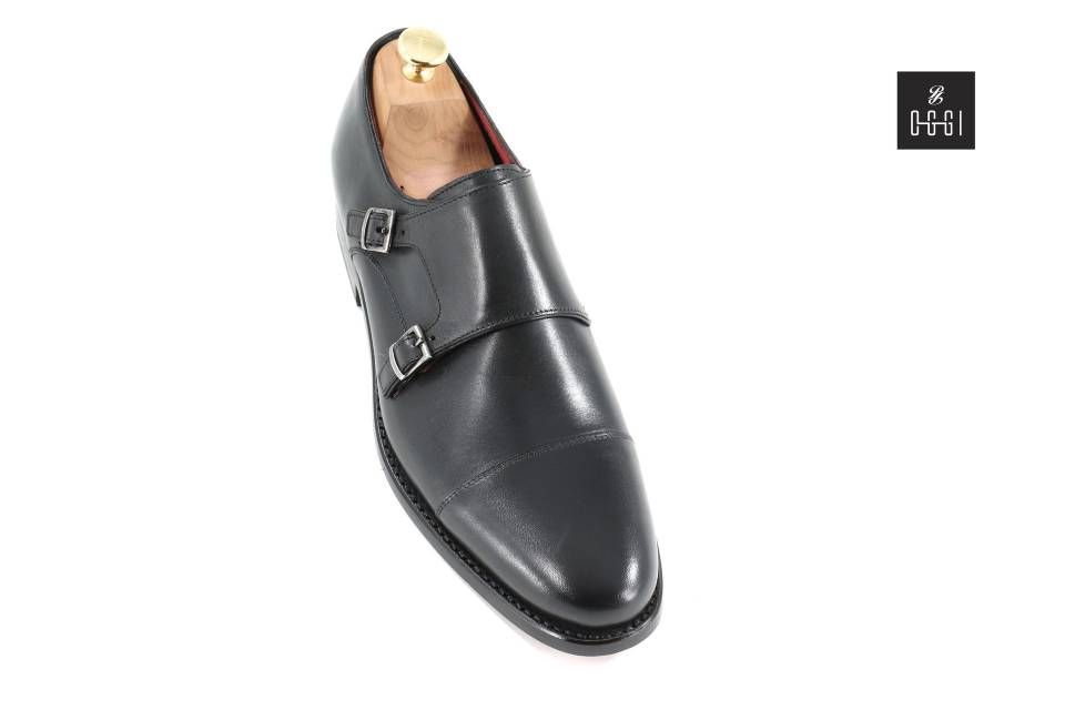 Une paire de chaussures noires à double boucle avec un porte-chaussures en bois.