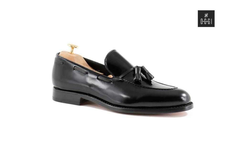 Une paire de mocassins noirs à pompons sur fond blanc.