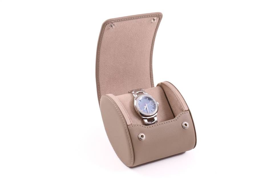 Une montre est posée dans un petit boîtier marron sur fond blanc.