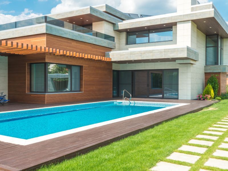 Casa moderna con piscina, rodeada de césped. La casa tiene una fachada de madera y piedra clara.