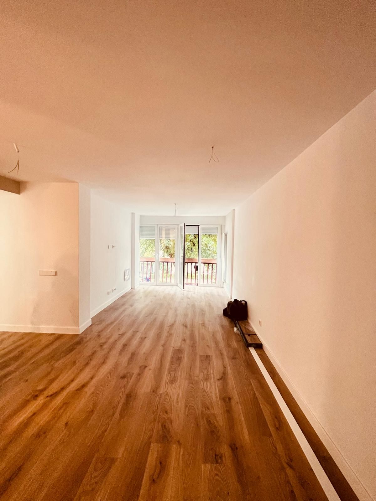 Una gran habitación vacía con suelos de madera y paredes blancas.