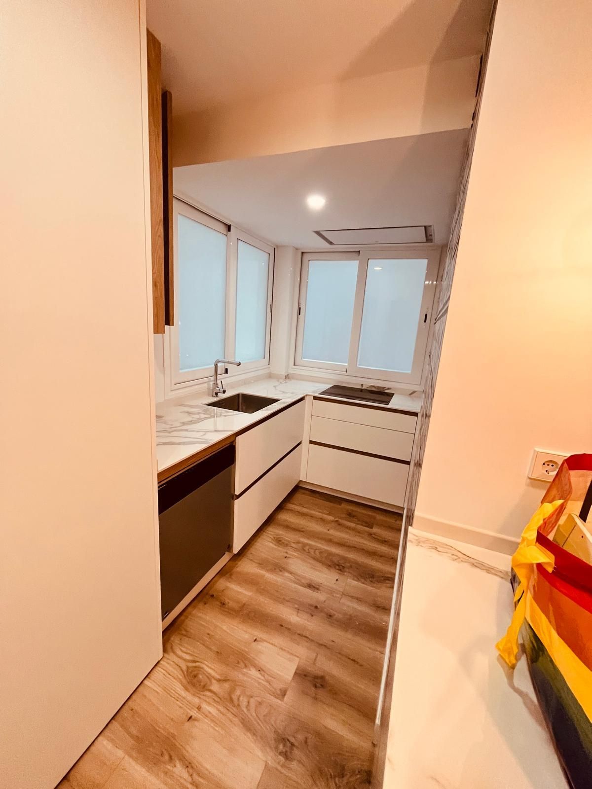 Una cocina con pisos de madera, gabinetes blancos, un fregadero y una ventana.