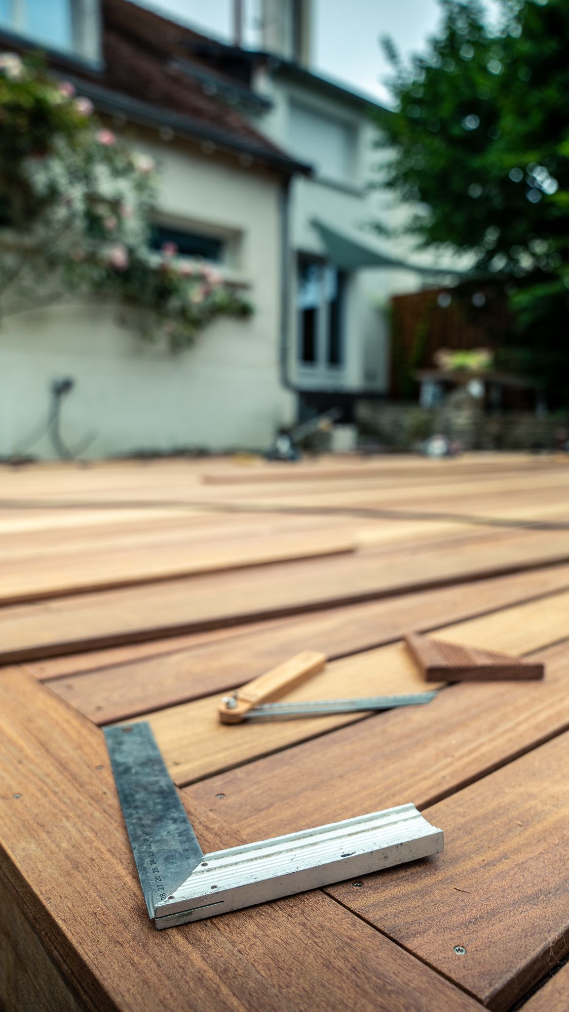 Outils carrés et d'angle sur une terrasse en bois en construction, arrière-plan flou d'une maison et de verdure.