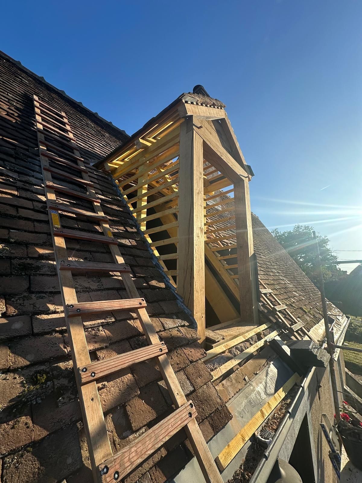 Toiture en construction avec nouvelle charpente bois. Tuiles brunes, ciel bleu.