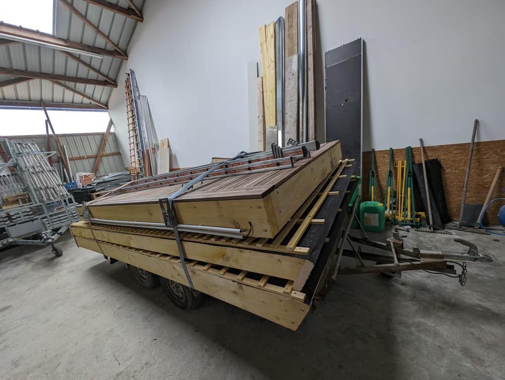 Une remorque chargée dans un entrepôt, transportant des panneaux de bois, des poutres métalliques et des outils.
