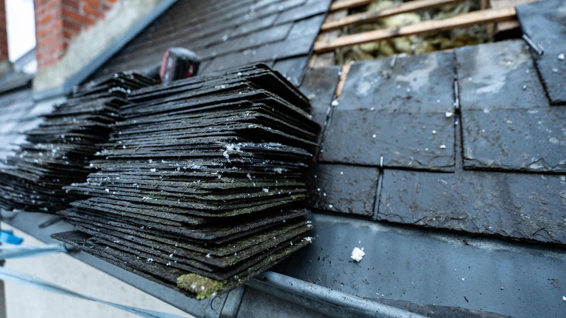 Pile de tuiles en ardoise à côté d'un toit partiellement exposé pendant la réparation.