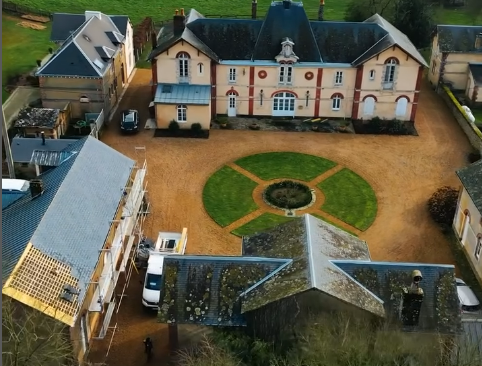 Vue aérienne d'un manoir avec un jardin circulaire, une cour en gravier et des bâtiments en cours de rénovation.