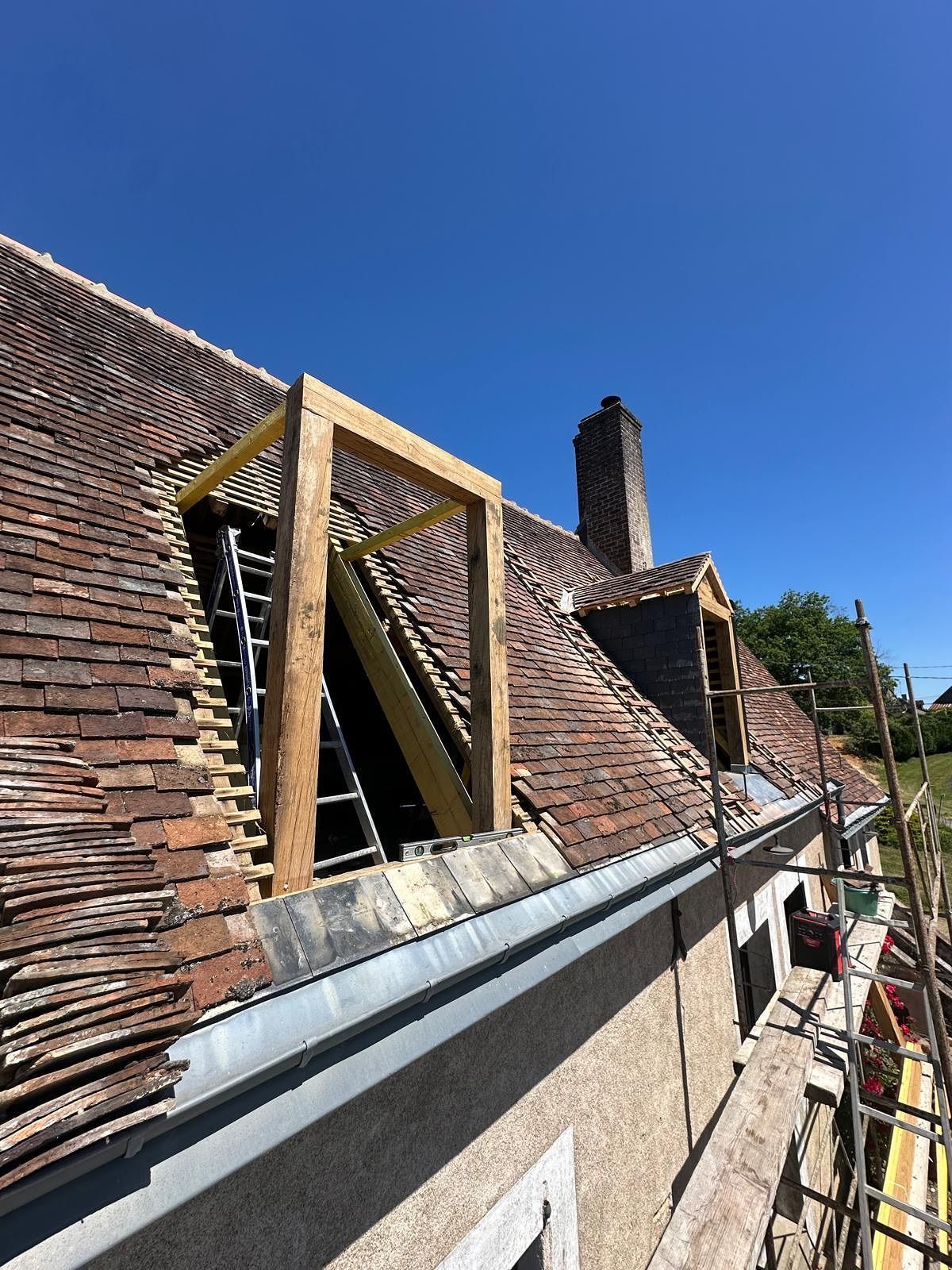 Toiture avec ossature en bois, cheminée et échelle en cours de construction par une journée ensoleillée.
