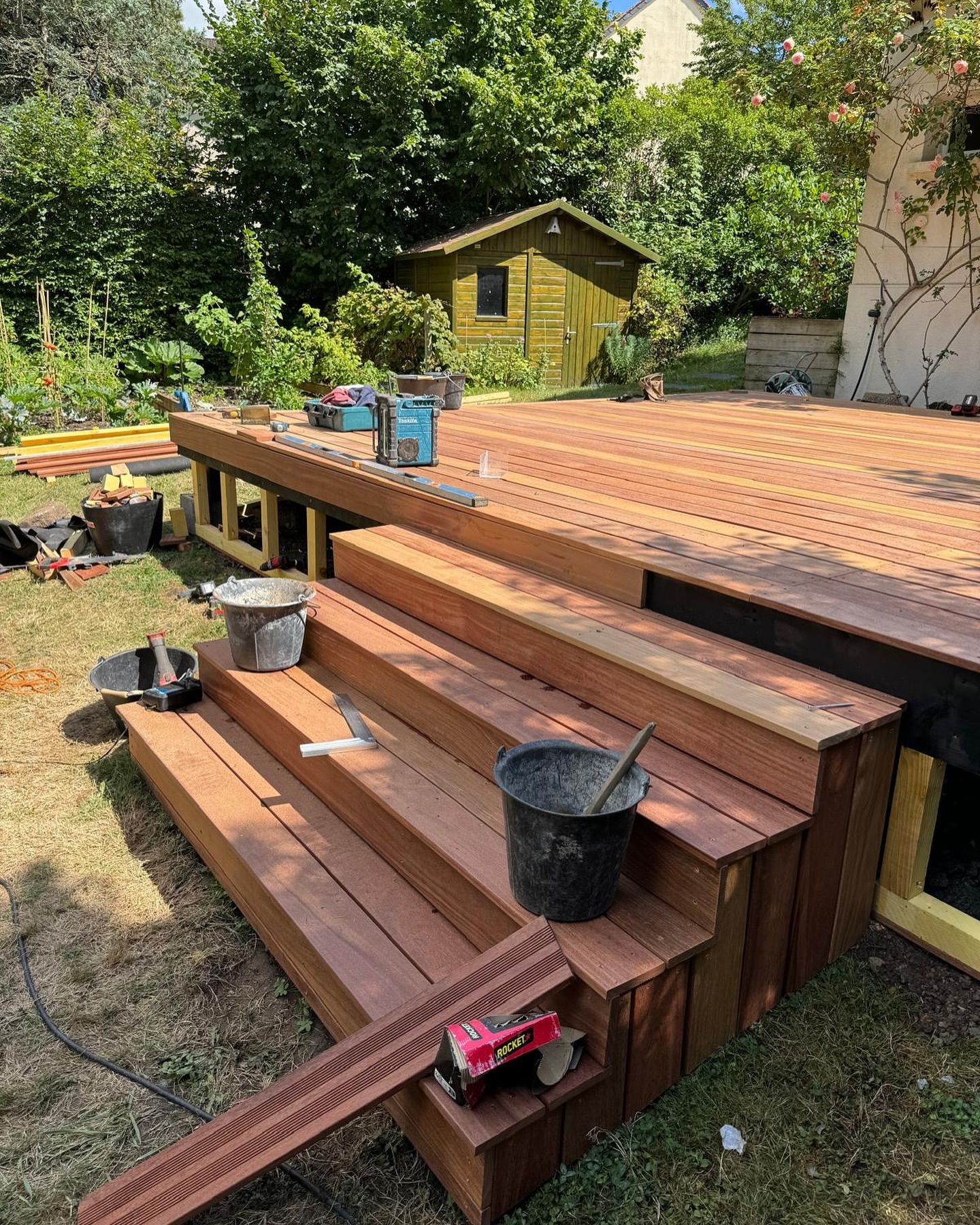 Terrasse et marches en bois en construction dans un jardin. Outils, seaux et abri de jardin inclus.