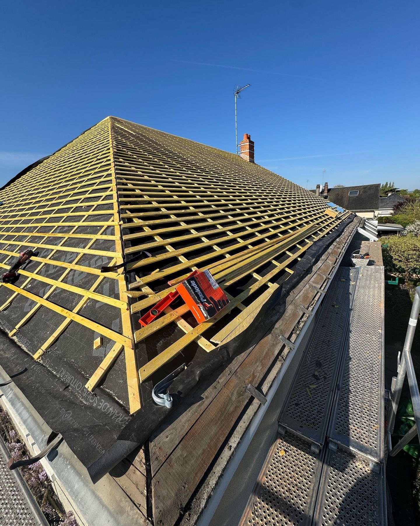 Toiture en construction avec poutres apparentes en bois et sous-couche foncée ; ciel bleu.
