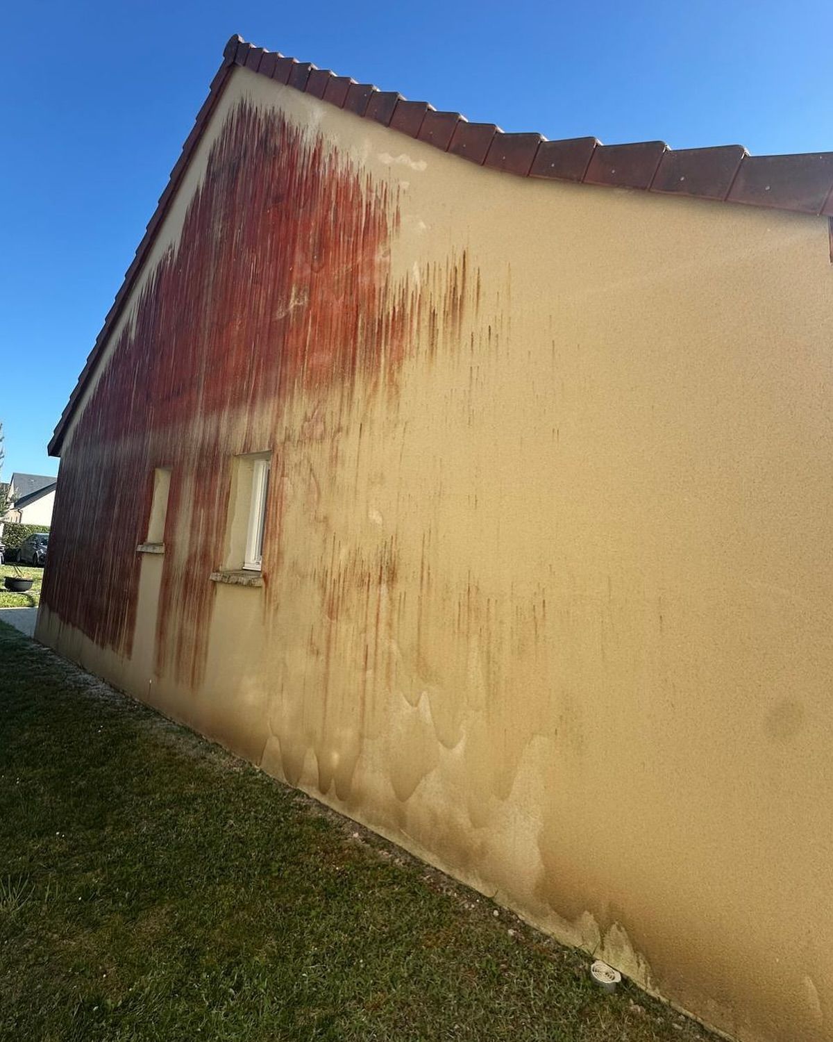 Côté d'une maison aux murs texturés rouge et beige, tachés de traces d'eau, avant nettoyage de façade.
