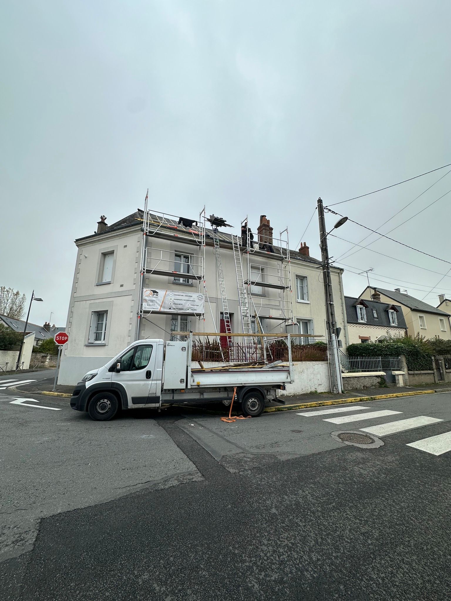 Camion blanc garé devant un bâtiment blanc avec échafaudage. Ciel nuageux.