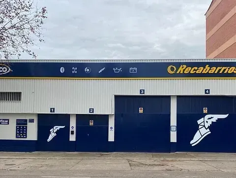 Exterior del taller mecánico de Recabarrios; edificio azul y blanco con puertas de garaje, logotipo y gráfico de un zapato con alas.